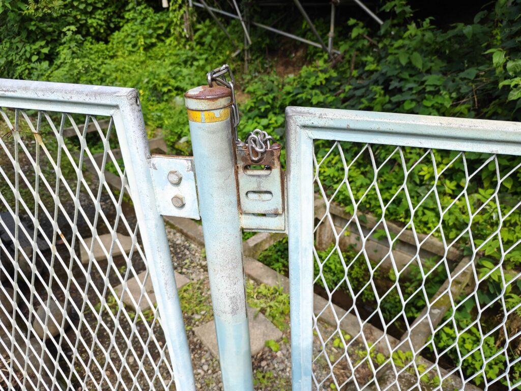 神奈川県秦野市にある峠の湧水へと降りていく場所の写真。フェンスを開けると階段がある。